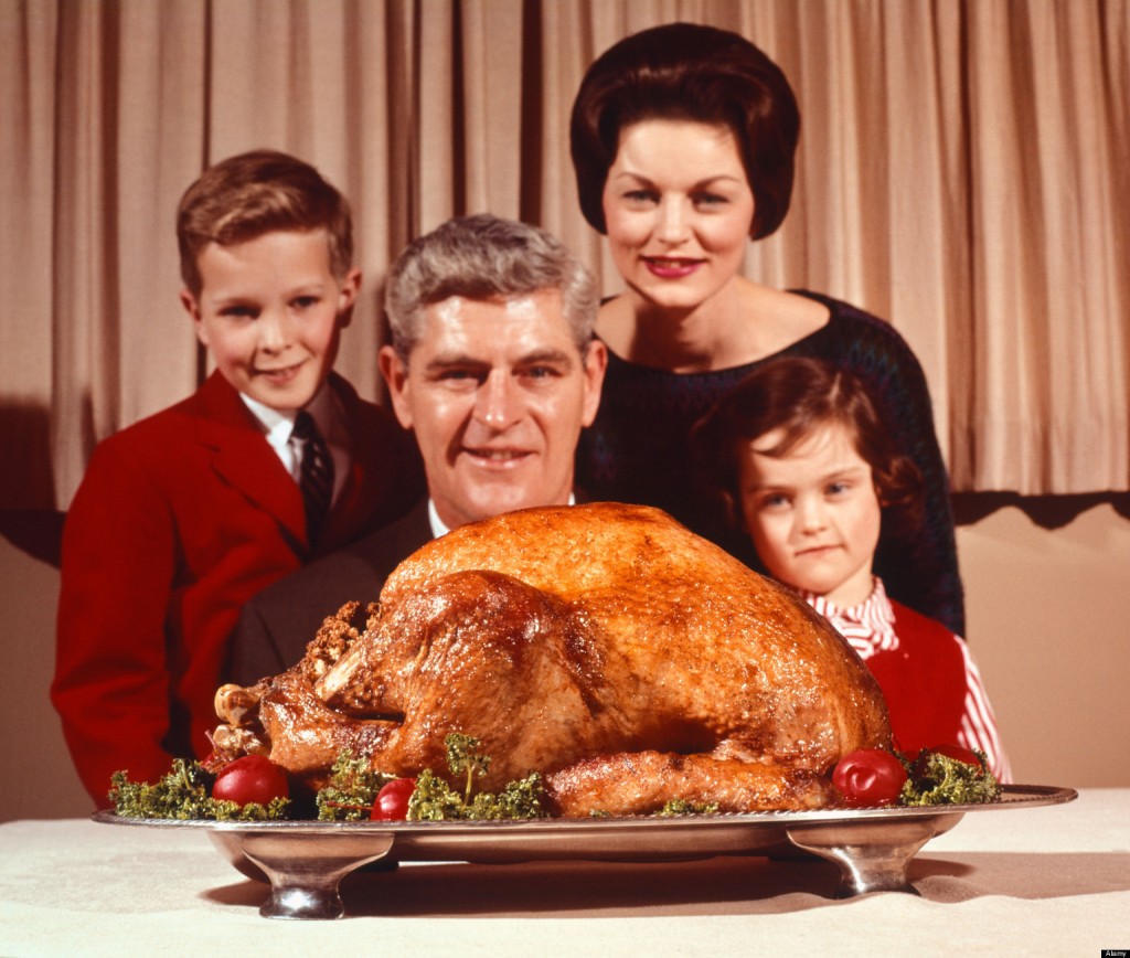 1960s PORTRAIT OF FAMILY FATHER MOTHER SON DAUGHTER LOOKING AT THANKSGIVING OR CHRISTMAS ROAST TURKEY
